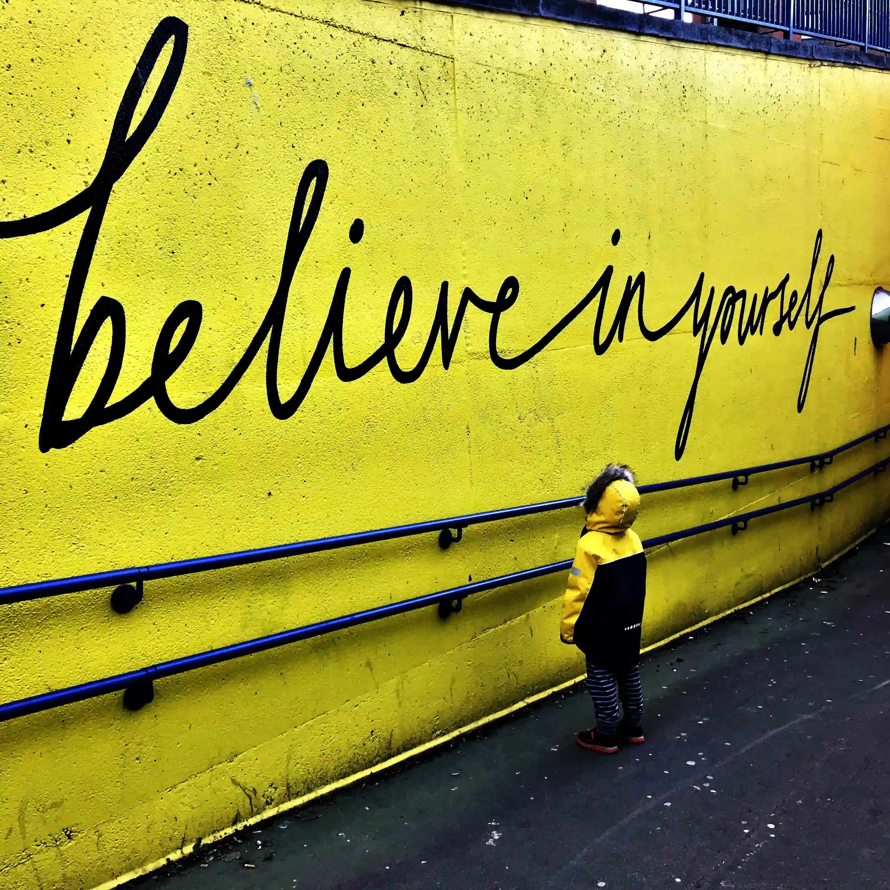 Kleiner Junge steht vor Schriftzug "Believe in yourself"
